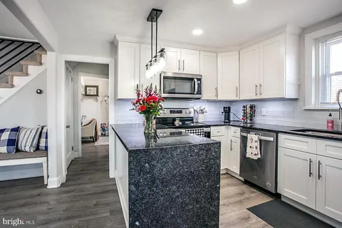 a kitchen with kitchen island granite countertop a stove a sink dishwasher and a microwave oven with white cabinets