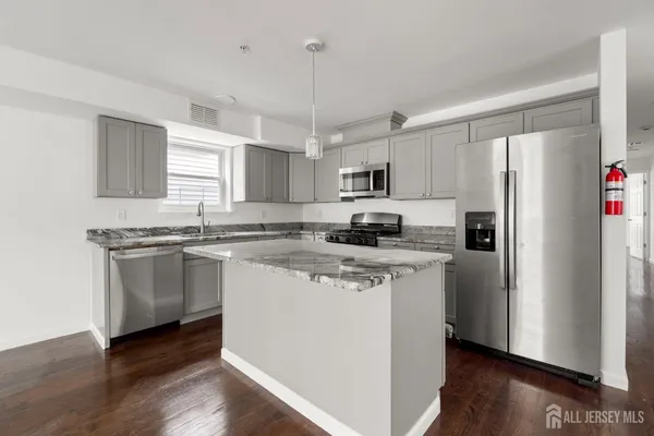 a kitchen with kitchen island granite countertop a refrigerator a sink dishwasher a stove and white cabinets with wooden floor