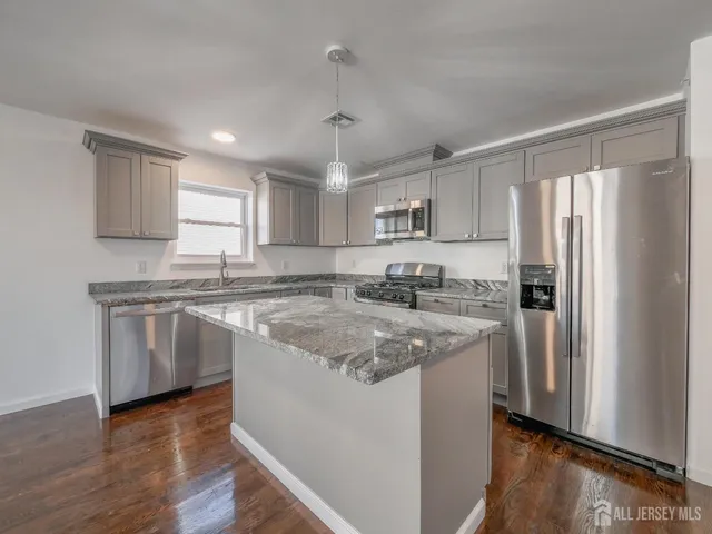 a kitchen with stainless steel appliances granite countertop a refrigerator a sink dishwasher a stove top oven a refrigerator and white cabinets with wooden floor
