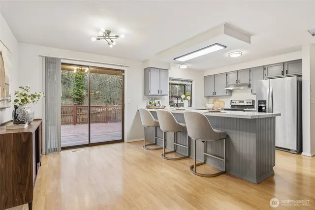 a kitchen with stainless steel appliances a refrigerator a sink dishwasher a dining table and chairs with wooden floor