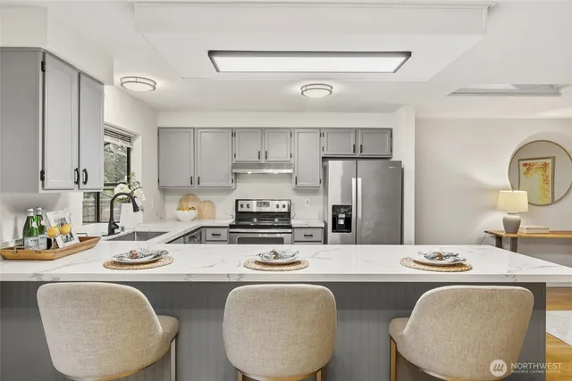 a kitchen with stainless steel appliances granite countertop a sink a stove a kitchen island with chairs and white cabinets