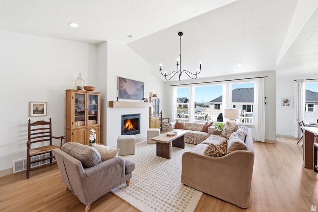 283 North 500 West Mapleton, UT 84664 - Photo 15 of 102 Living room with lofted ceiling, a chandelier, a warm lit fireplace, light wood-style floors with large windows.