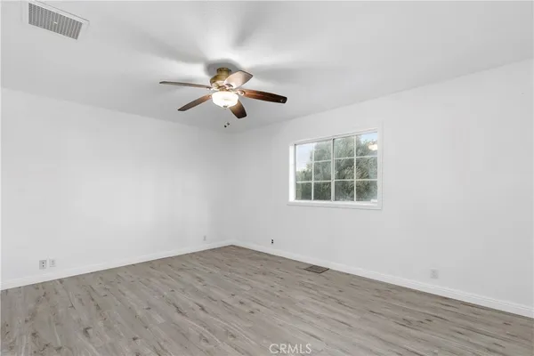 an empty room with wooden floor ceiling fan and windows