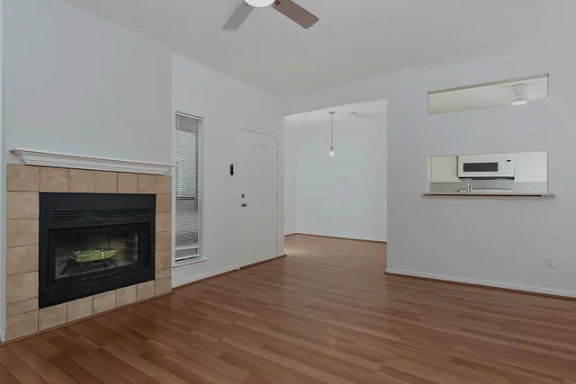 a view of an empty room with wooden floor fireplace and a window