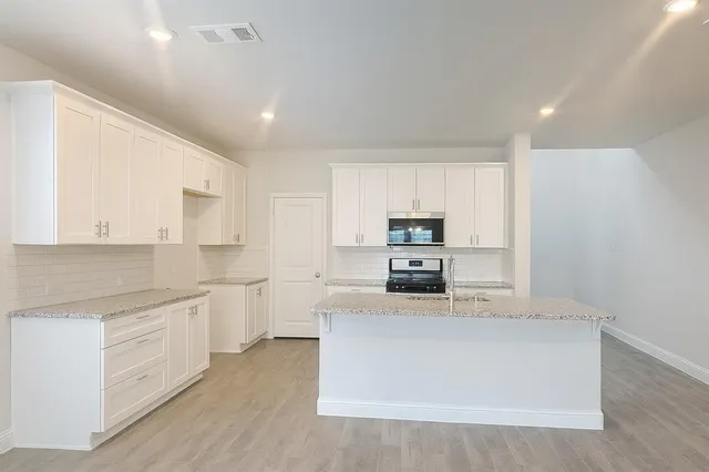 a kitchen with stainless steel appliances a sink a stove a microwave a center island and cabinets