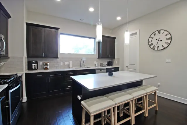 a kitchen with stainless steel appliances granite countertop a sink a stove a refrigerator cabinets and a dining table