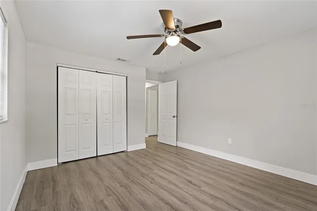 an empty room with wooden floor fan and windows
