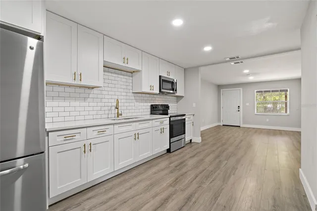 a kitchen with granite countertop a stove a sink a refrigerator and white cabinets with wooden floor