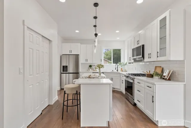 a kitchen with stainless steel appliances granite countertop a stove top oven a sink dishwasher a refrigerator and white cabinets with wooden floor