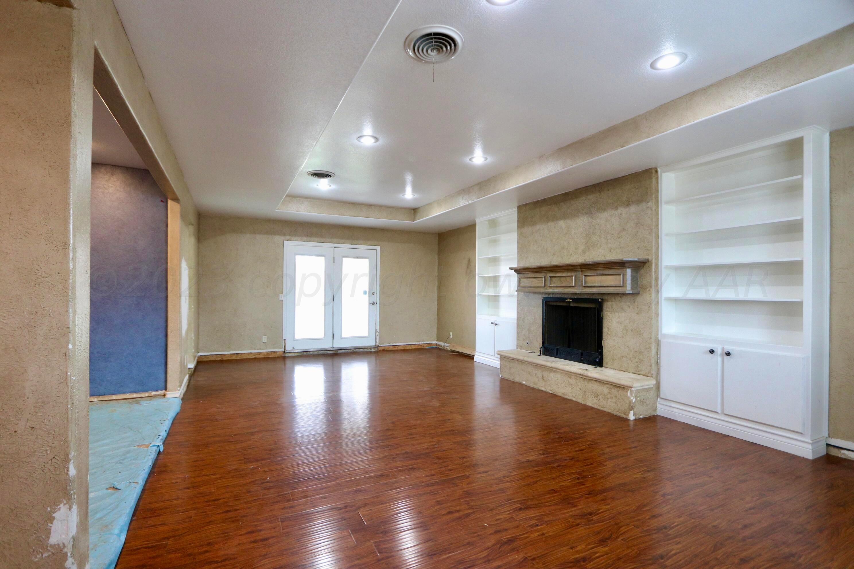 7916 Fenley Drive Amarillo, TX 79121 - Photo 5 of 23 an empty room with wooden floor a fireplace and windows