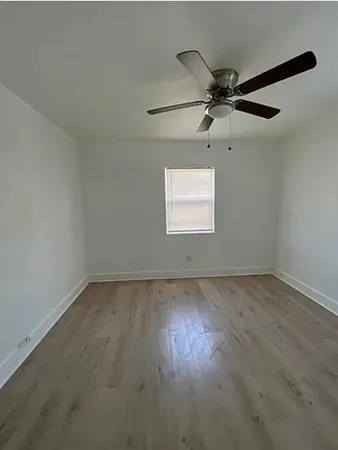 an empty room with wooden floor ceiling fan and windows