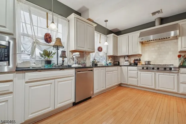 a kitchen with stainless steel appliances white cabinets a sink and a wooden floor