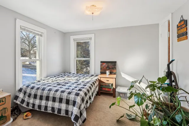 a bedroom with a bed table flowerpot and a window