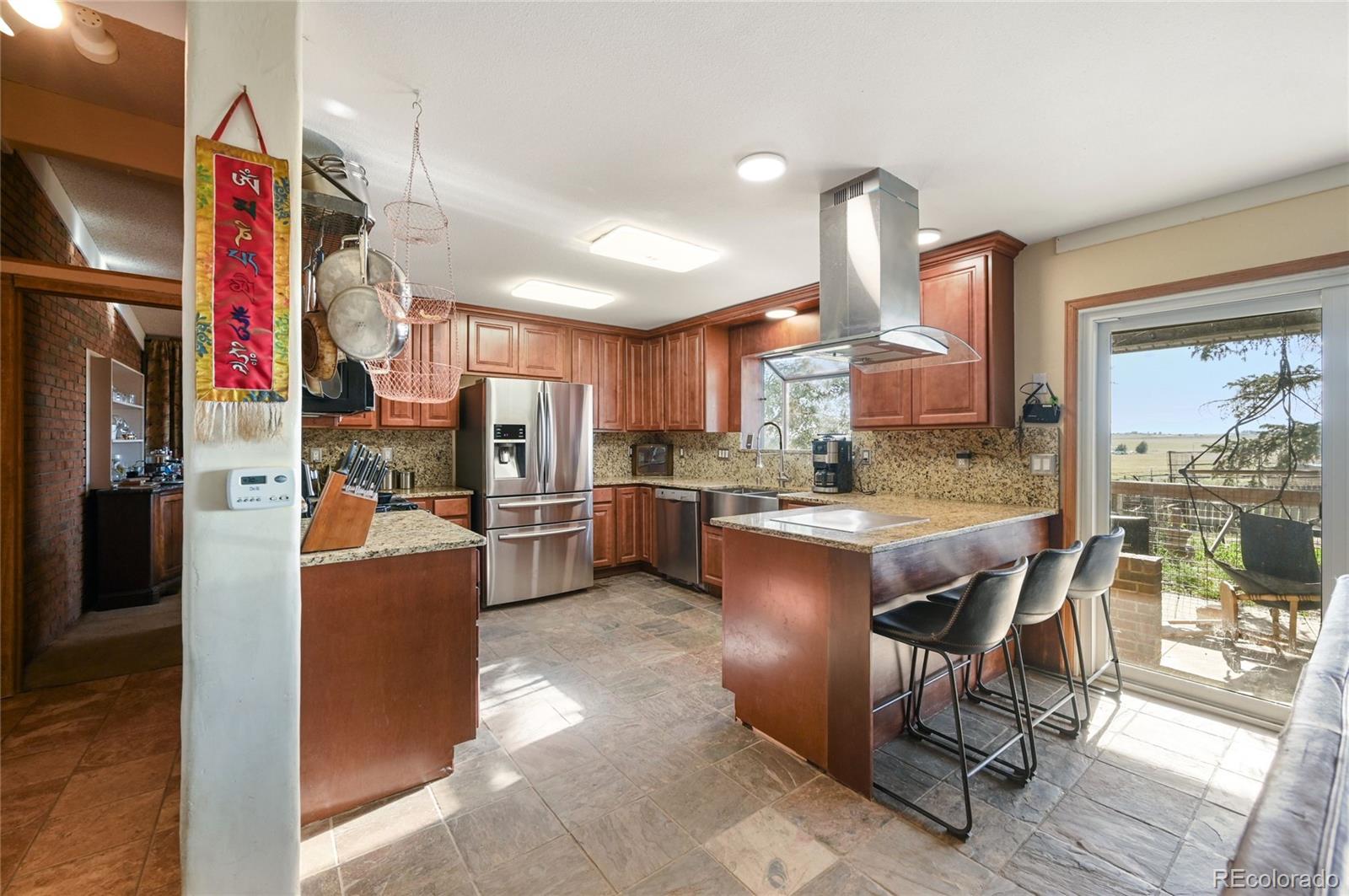 5430 Murr Road Peyton, CO 80831 - Photo 37 of 50 a kitchen with stainless steel appliances kitchen island granite countertop a refrigerator a oven a sink a dining table and chairs with wooden floor