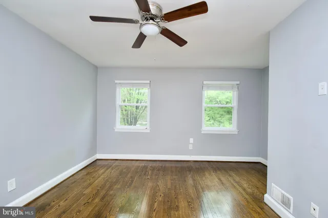 an empty room with wooden floor fan and windows