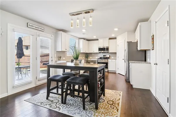 a kitchen with stainless steel appliances granite countertop a dining table chairs refrigerator and cabinets