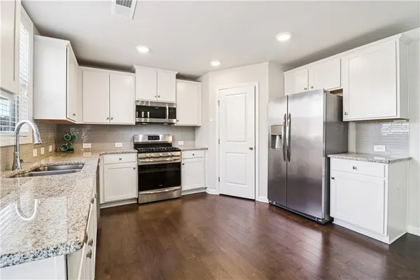 a kitchen with granite countertop a refrigerator a stove top oven a sink and dishwasher with wooden floor