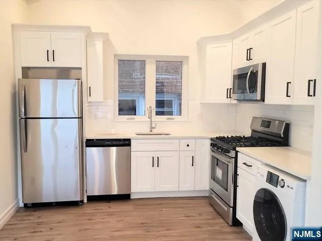 a kitchen with stainless steel appliances granite countertop a refrigerator a stove a sink and white cabinets