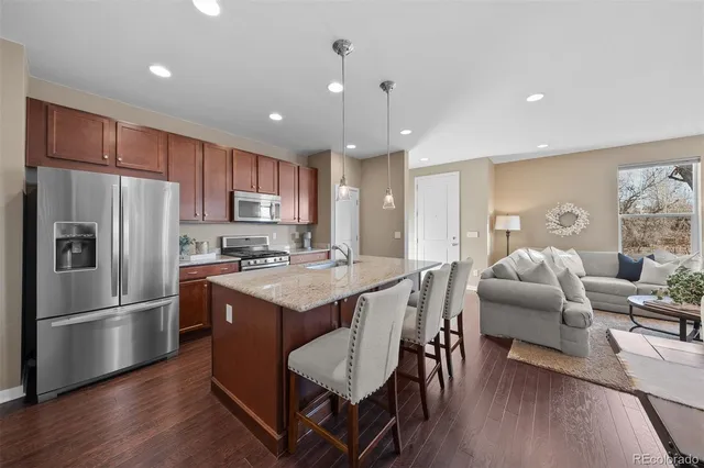 a kitchen with stainless steel appliances granite countertop a refrigerator a sink dishwasher a dining table and chairs with wooden floor