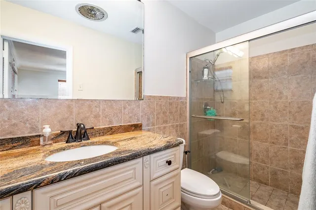 a bathroom with a granite countertop sink a toilet a mirror and shower