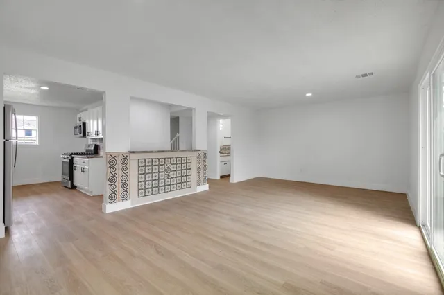 a view of an empty room with wooden floor and a kitchen