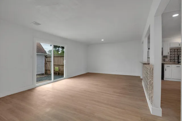 a view of an empty room with wooden floor and a kitchen
