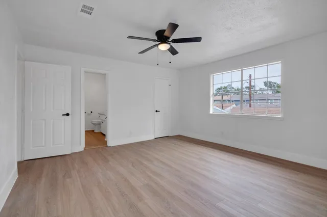 an empty room with wooden floor ceiling fan and windows