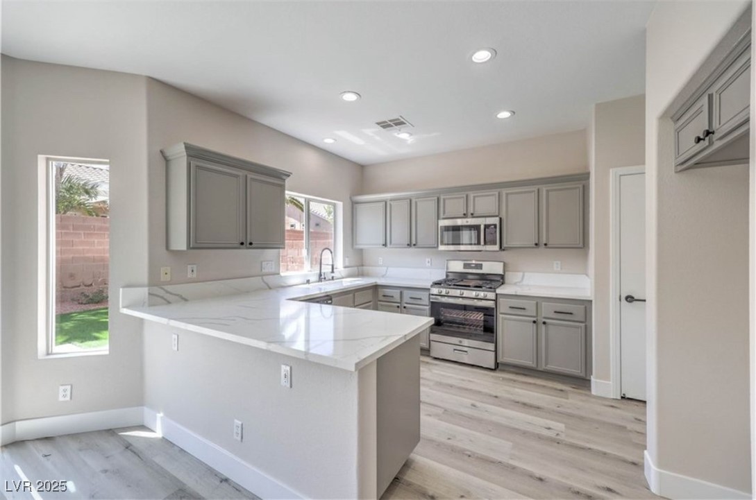 979 Park Bridge Avenue Las Vegas, NV 89123 - Photo 14 of 57 Kitchen with gray cabinetry, appliances with stainless steel finishes, a peninsula, light wood-style flooring, and recessed lighting