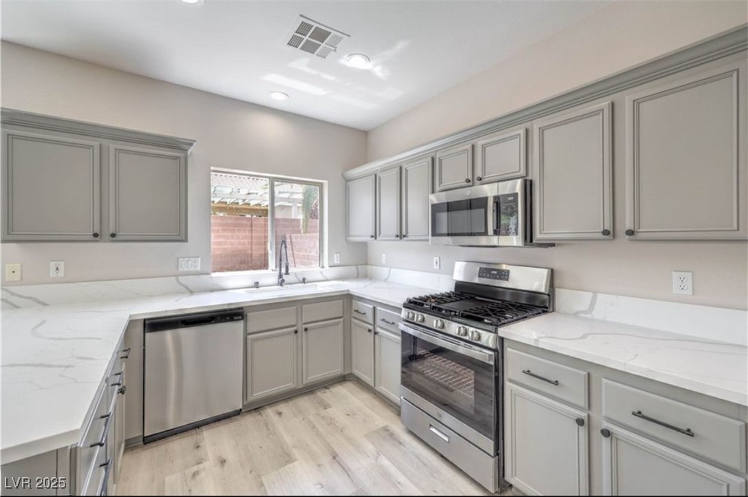 979 Park Bridge Avenue Las Vegas, NV 89123 - Photo 15 of 57 Kitchen featuring gray cabinets, appliances with stainless steel finishes, light wood-type flooring, light stone counters, and recessed lighting