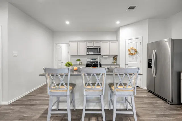 a kitchen with stainless steel appliances a dining table chairs refrigerator and microwave