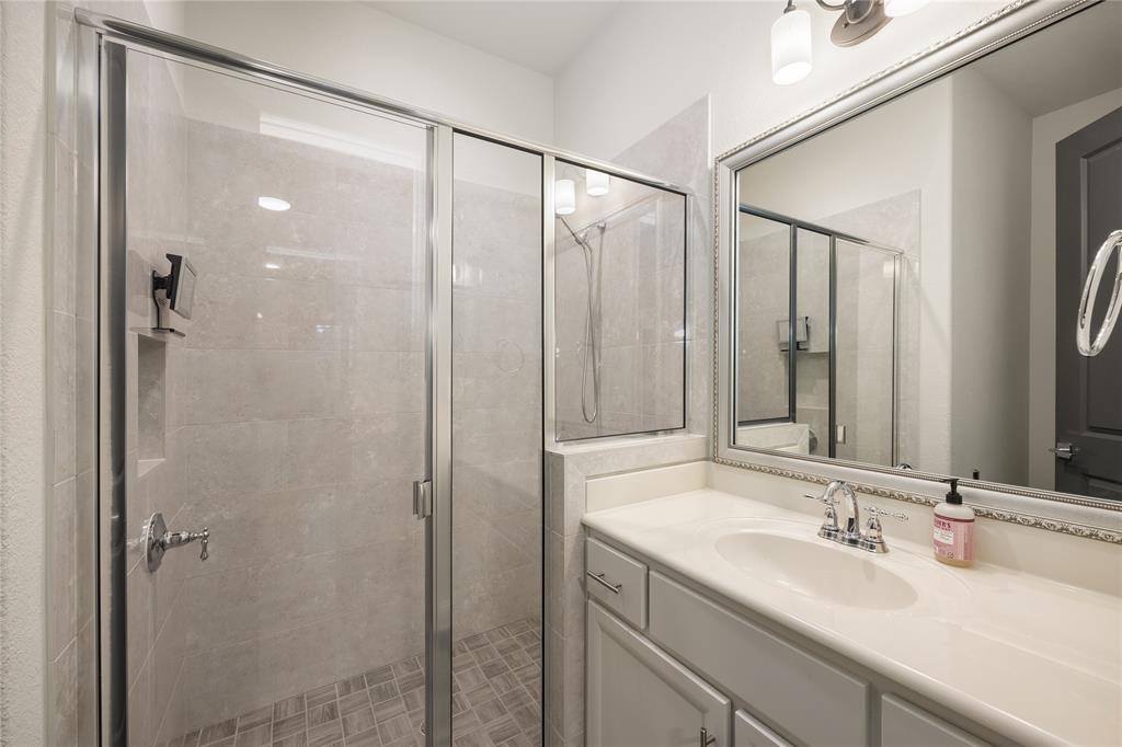 918 Sydney Lane Allen, TX 75013 - Photo 21 of 40 Guest Bathroom with a glass-enclosed shower featuring tiled walls and floor, alongside a vanity with a white countertop, an oval sink, and a framed mirror