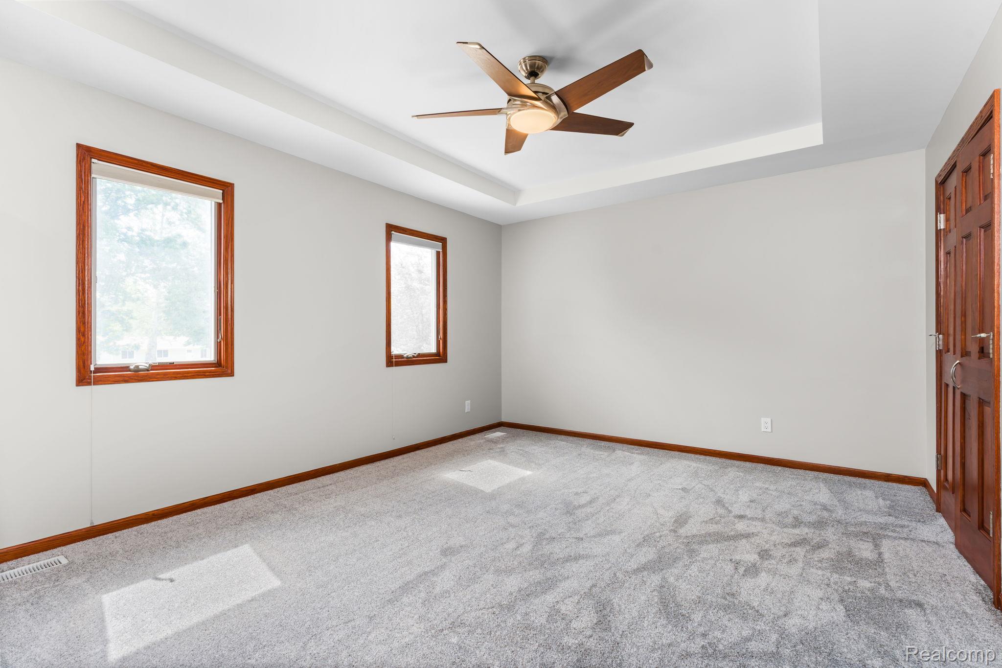 2381 Burke Road Fowlerville, MI 48836 - Photo 15 of 31 Spacious room with tray ceiling, modern ceiling fan, two windows with wood trim, neutral wall color, and plush gray carpeting