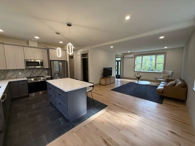 a large kitchen with stainless steel appliances kitchen island granite countertop a refrigerator a stove a sink a dining table and chairs with wooden floor