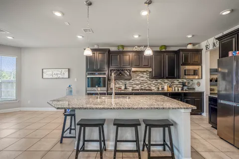 a kitchen with stainless steel appliances kitchen island granite countertop a table chairs sink and microwave