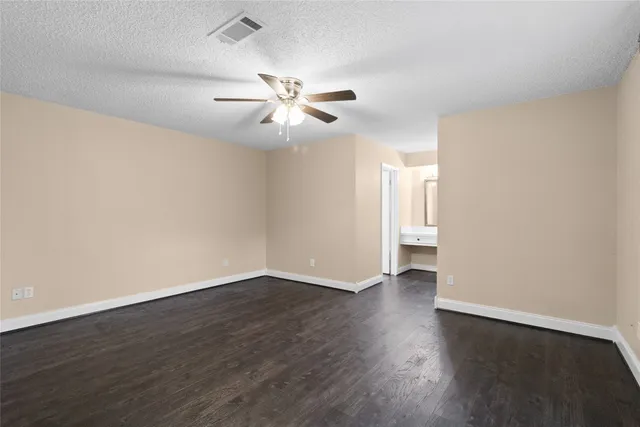 a view of an empty room with wooden floor and a ceiling fan