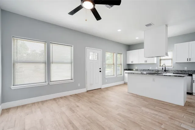 a large kitchen with stainless steel appliances granite countertop a stove a sink and white cabinets with wooden floor