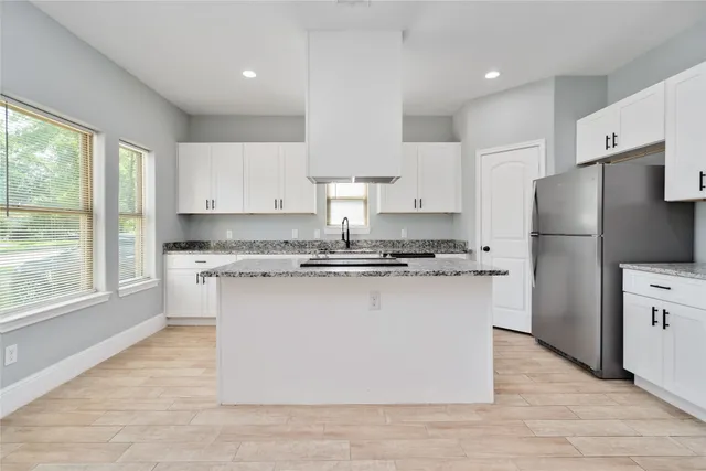 a kitchen with stainless steel appliances granite countertop a refrigerator a sink dishwasher a stove and white cabinets with wooden floor