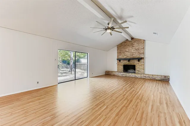 an empty room with wooden floor fireplace and windows