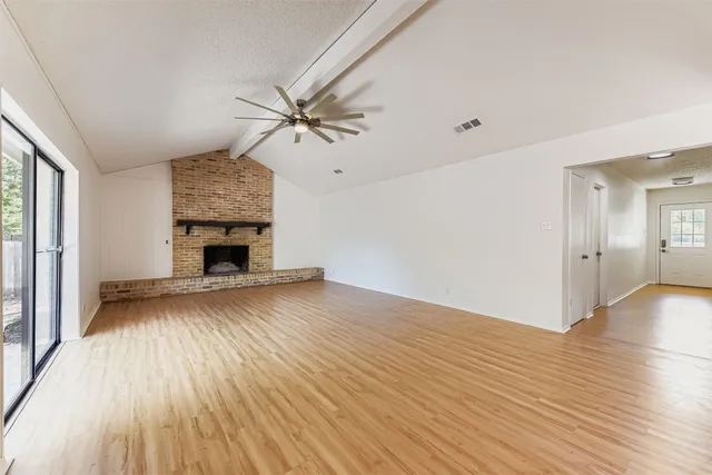 an empty room with wooden floor fireplace and windows