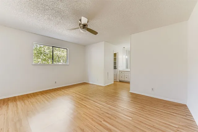 an empty room with wooden floor chandelier fan and windows