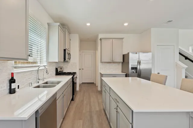 a large kitchen with stainless steel appliances a sink dishwasher a refrigerator and white cabinets with wooden floor