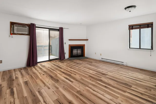 a view of an empty room with wooden floor fireplace and a window