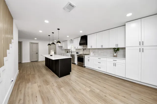 a large kitchen with stainless steel appliances kitchen island a sink dishwasher a refrigerator and white cabinets with wooden floor