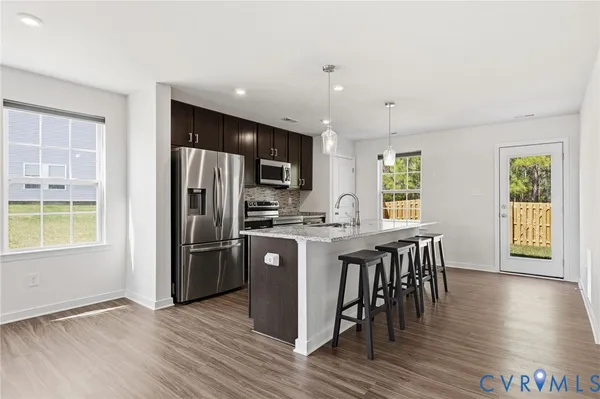 a kitchen with stainless steel appliances granite countertop a refrigerator a sink dishwasher a stove and a dining table with wooden floor