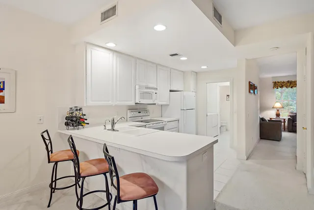 a white kitchen with a stove a sink and white cabinets with wooden floor