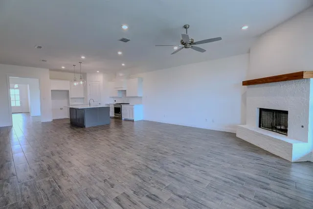 an empty room with wooden floor fire place and kitchen view