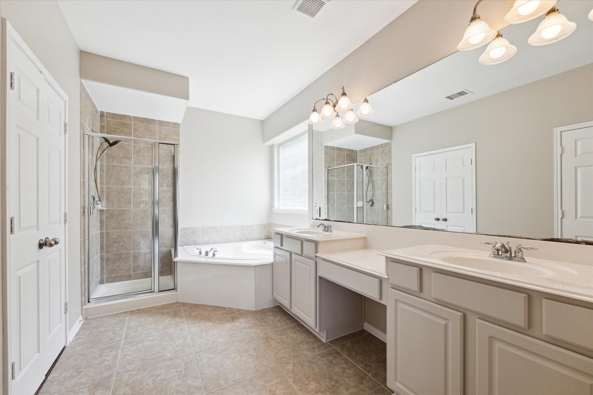 30507 Russell Point Drive Spring, TX 77386 - Photo 15 of 33 The primary bathroom features a spacious layout with shower, a large bathtub, dual sinks with ample counter space, elegant lighting fixtures, and neutral tile flooring.