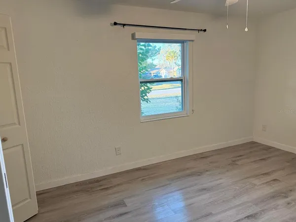 a view of an empty room with wooden floor and a window