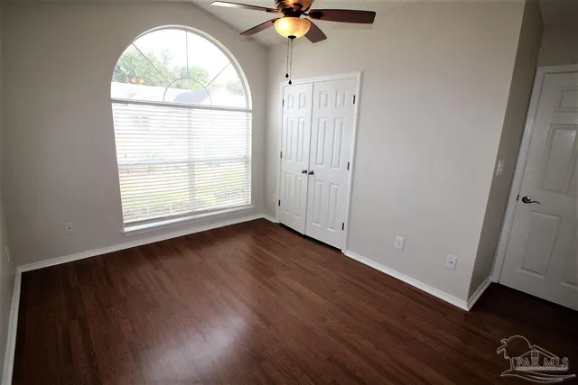 an empty room with wooden floor chandelier fan and windows