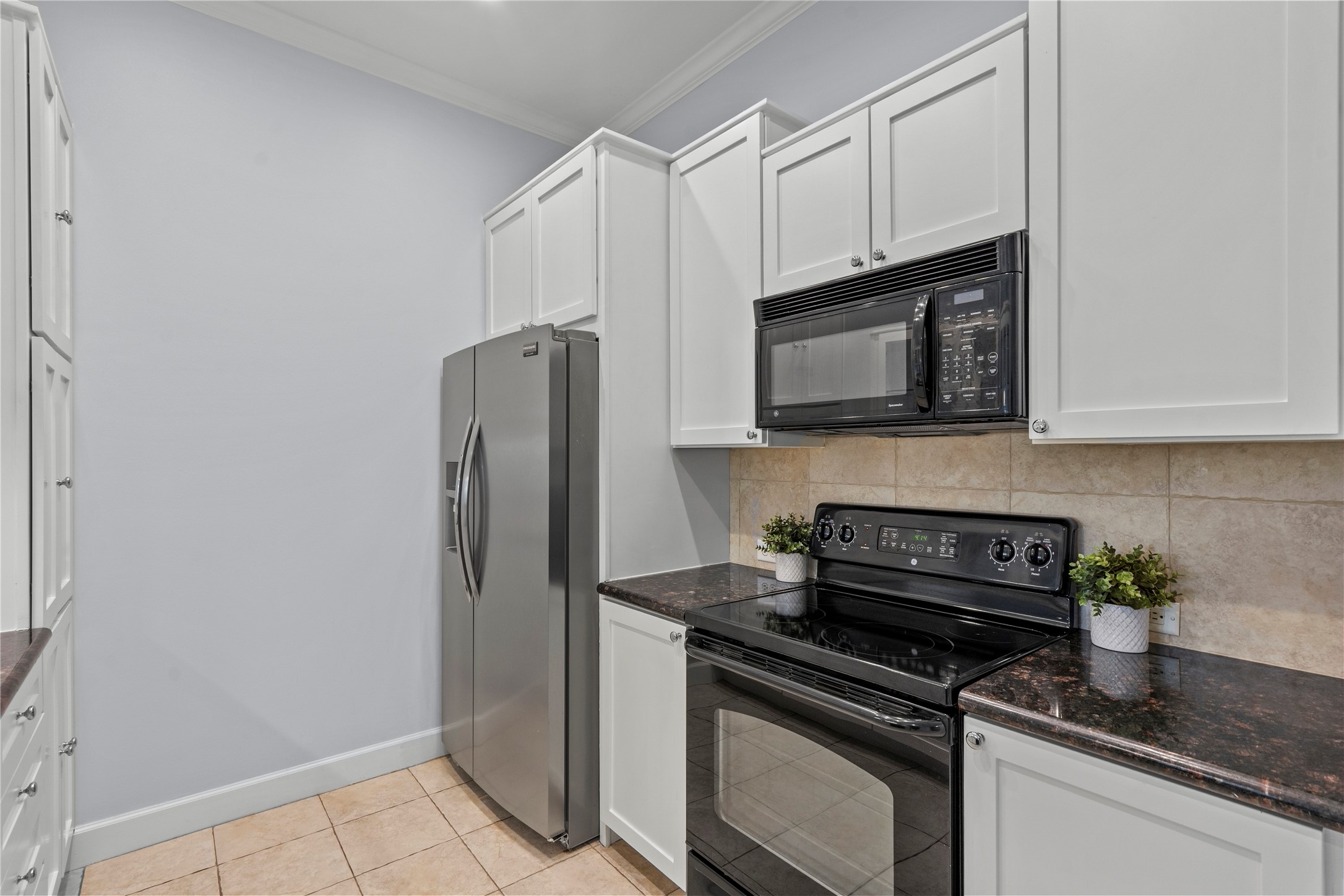 1900 Genesee Street, Unit 203 Houston, TX 77006 - Photo 12 of 30 This kitchen features modern stainless steel refrigerator, sleek black countertops, white cabinetry, and a tiled backsplash, offering a clean and contemporary look.